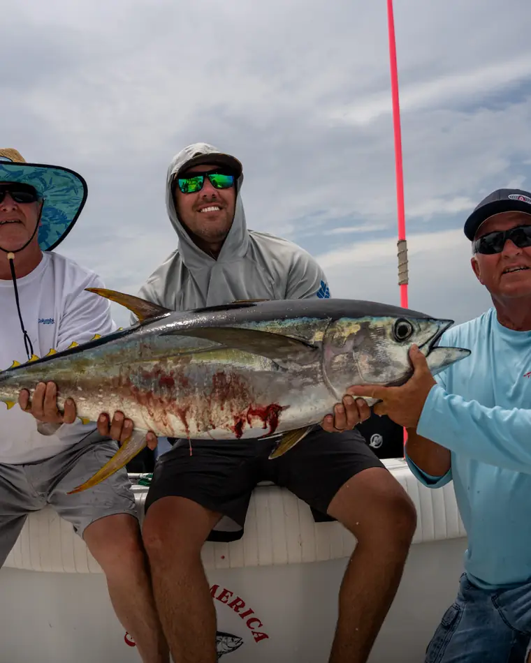 Three anglers holding a yellowfin tuna offshore
